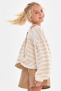 A girl wearing a cream and taupe fine horizontal stripe brushed knit pullover top with a crew neckline, long sleeves with slightly flared cuffs, and a relaxed fit.