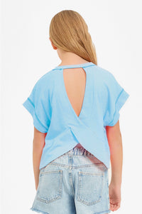 A girl wearing a neon coral sleeveless boxy crop top with a crew neckline and visible contrast overlock stitching along the armholes, side seams, and hem, paired with light-wash denim shorts.